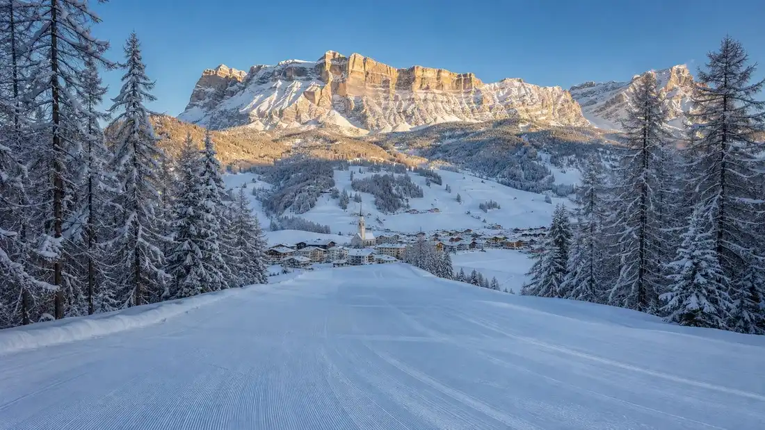 Upravená sjezdovka klesající k ladinské vesnici v Alta Badii pod stěnami Dolomit