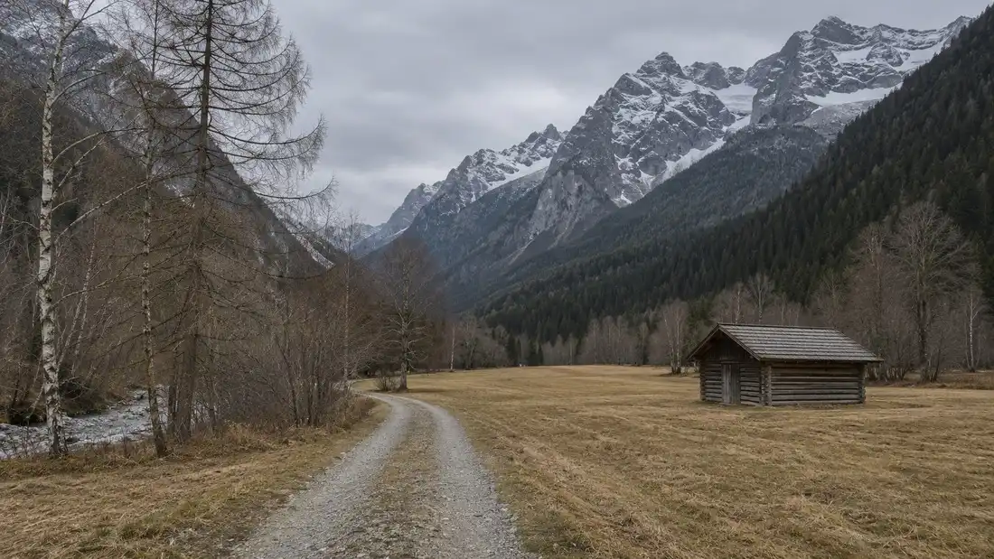 Holé podzimní údolí v Pustertalu bez sněhu a bez listí, zavřená chata u šotolinové cesty a první sníh na skalních stěnách